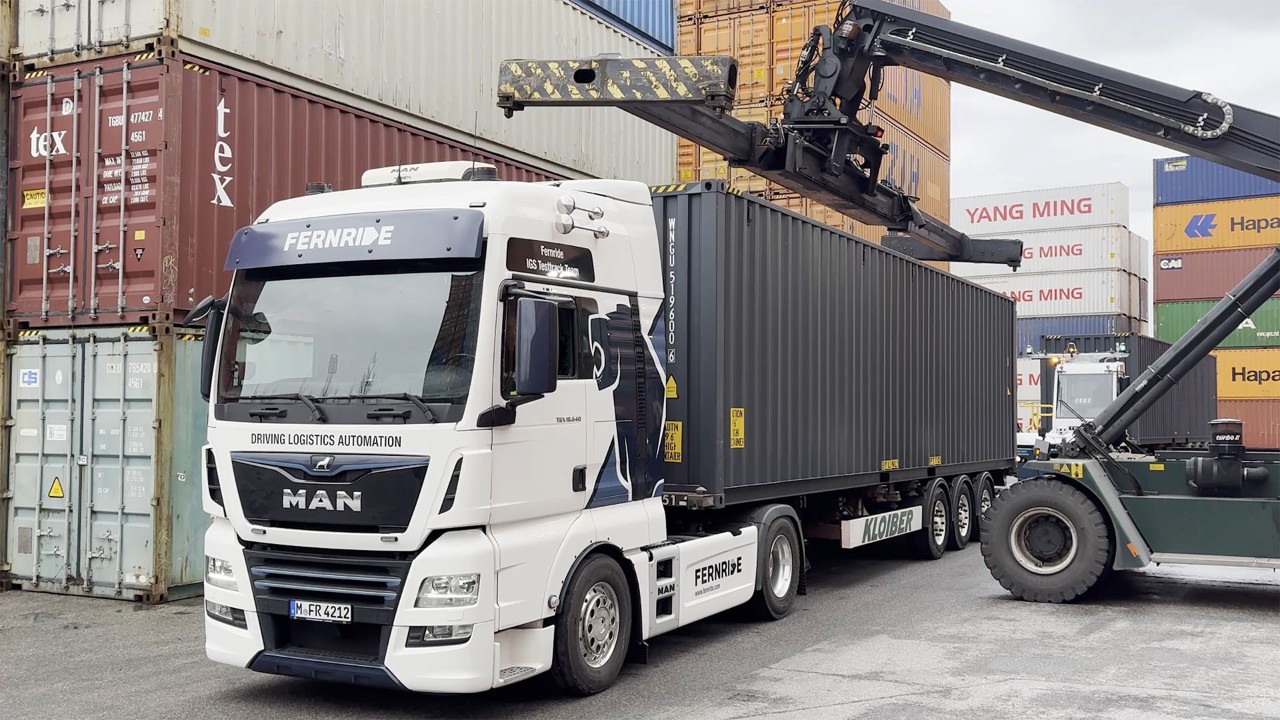 A crane lifts a large metal freight container onto the back of a waiting truck